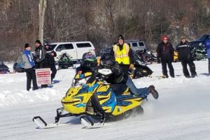A picture of a snow mobile rider, with people watching behind him.