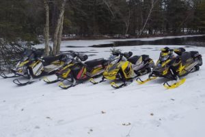 A picture of 4 snow mobiles in front of the water.
