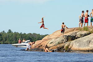 An image of boys jumping off rocks into the lake.