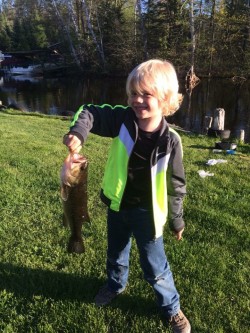 A picture of a boy holding a fish on the bank.
