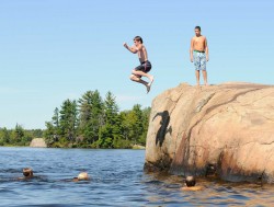 A picture of a group of boys jumping off of rocks and swimming in the water.