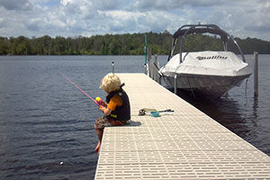 An image of a boy fishing while sitting on a dock.