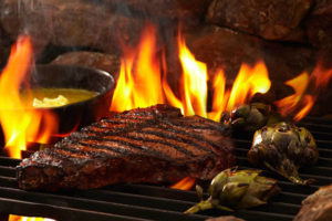 An image of a steak and artichokes over a flame. grill
