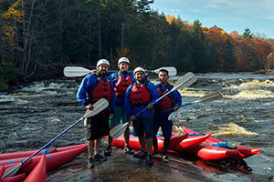 An image of 4 kayakers standing on a rock in the middle of the river.